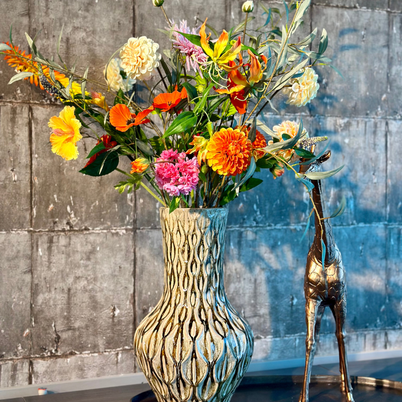 Boeket Beau van BloomFever in de stijlvolle keramiek vaas Inga Boa Beige met zijden bloemen zoals anjer, klaproos en gerbera op een schaal van brons met een bronzen giraffe als decoratie