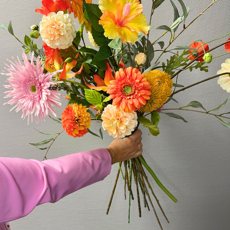 Hand die het kleurrijke zijden boeket Aayushi vasthoudt, met bloemen zoals dahlia's, gerbera's, gloriosa lelies en hibiscus van BloomFever