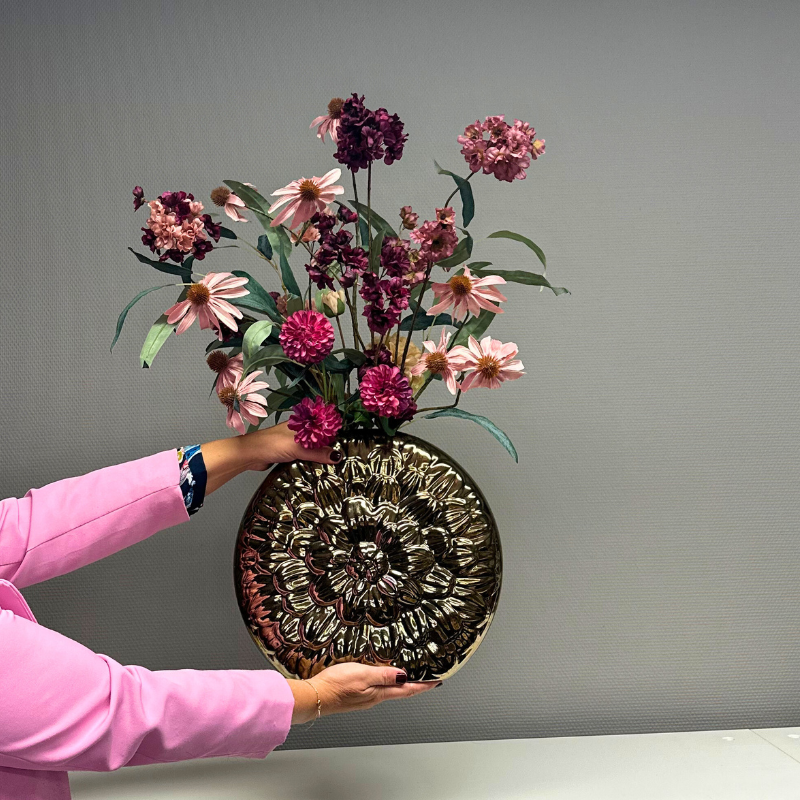 Zijden bloemenboeket genaamd Maddi, met een mix van levendige roze en paarse bloemen zoals echinacea's en anjers, aangevuld met subtiele groene bladeren. Het boeket wordt gepresenteerd in de een luxe gouden vaas met bloemendessin, genaamd Tobago Gold 35 x 31. Perfect passend bij de warme tinten van de herfst en winter.